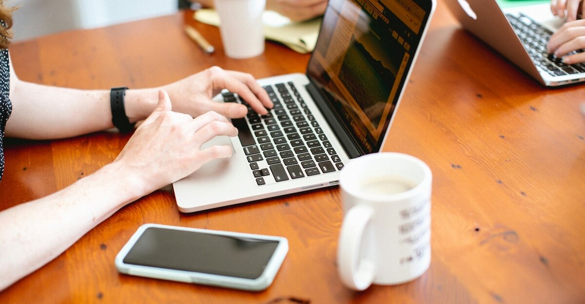 a profesional types on their laptop with their phone and coffee mug nearby