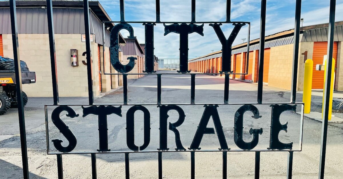 a gate displays the text"City Storage" in iron wrought, likely the name of the self storage company with self storage units in the background