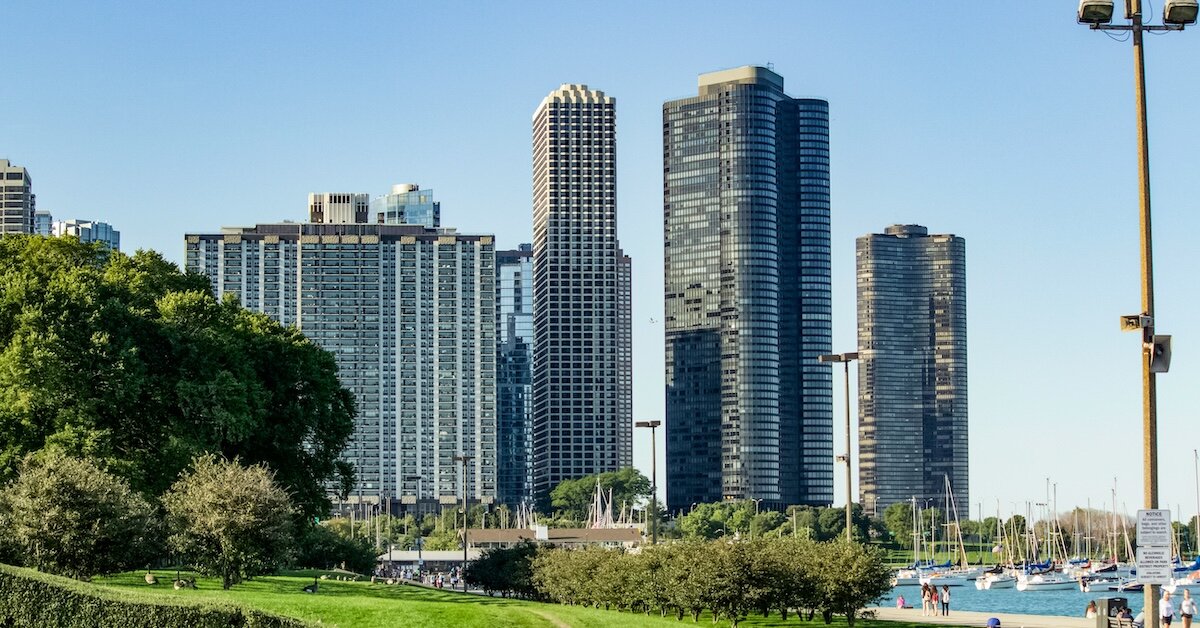 A downtown city skyline stands behind a lush green park and harbor in the foreground