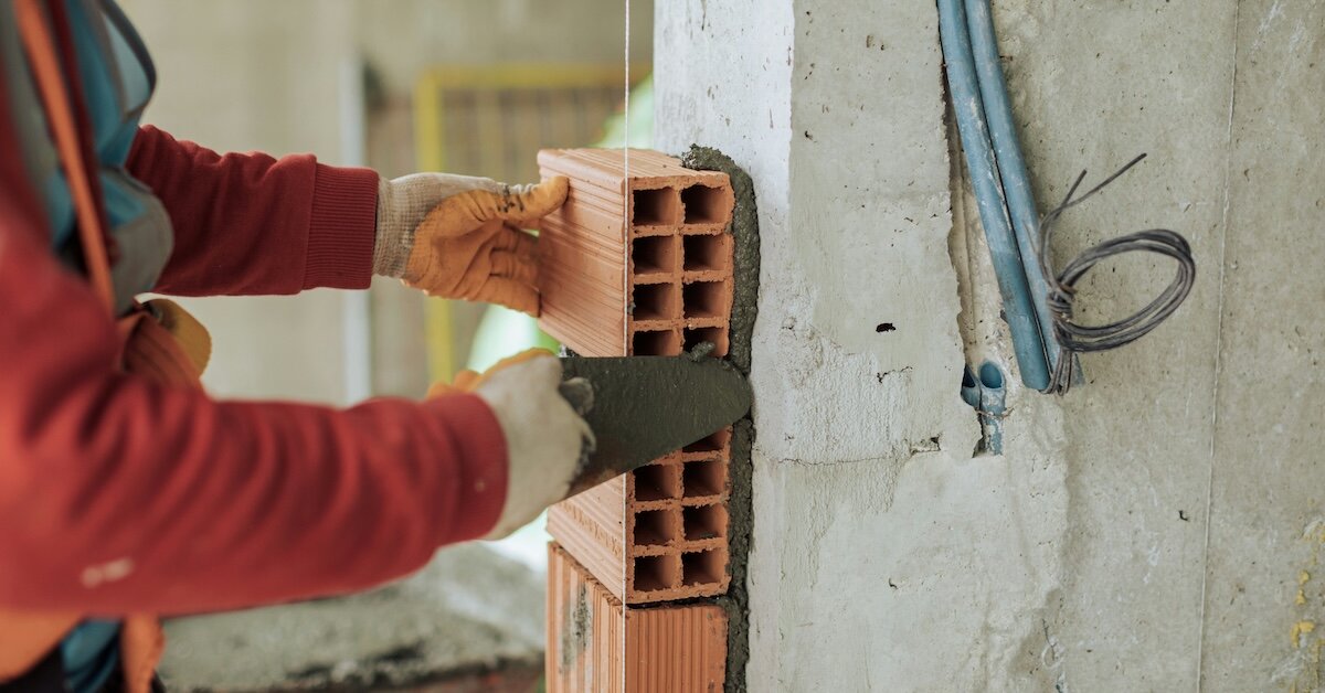 a construction worker affixing bricks to the outside of a building