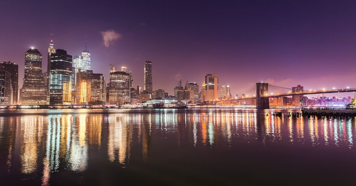 a downtown city at night, with the lights reflecting of the nearby water