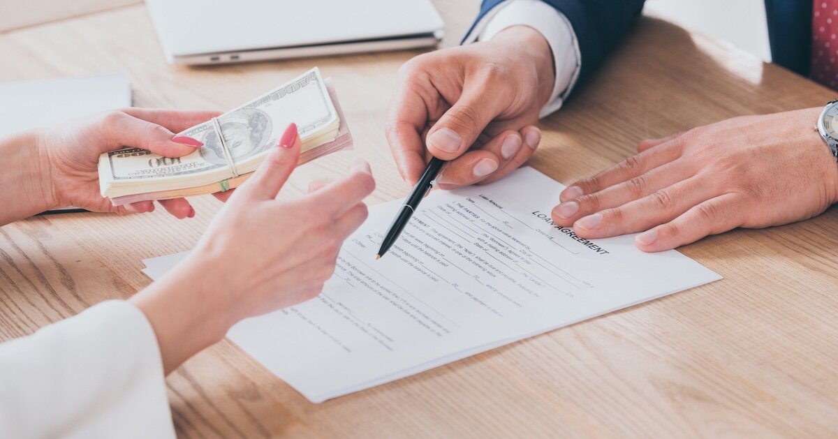A woman holds a bundle of cash while reviewing a contract presented by a businessman