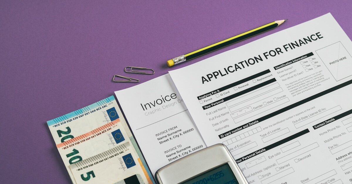 A loan application sits atop a pile with calculator, money, and invoice documentation