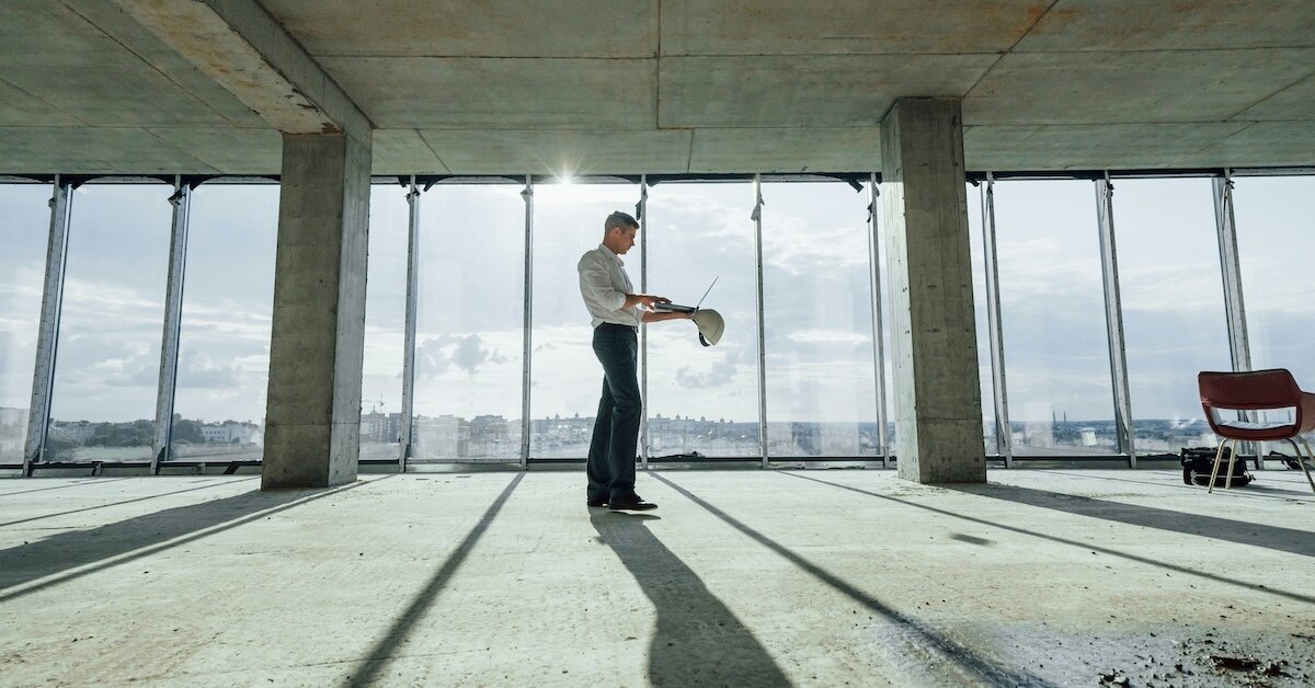 A person with a hard hat works on his computer at the top of an empty office building