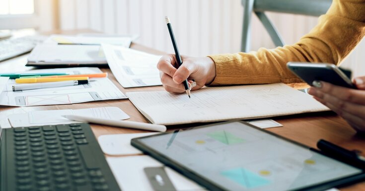 A woman makes notes at a crowded desk as she researches loan information