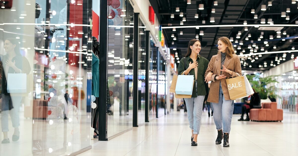 Two women walk down an indoor mall corridor with retail shoppig bags in hand