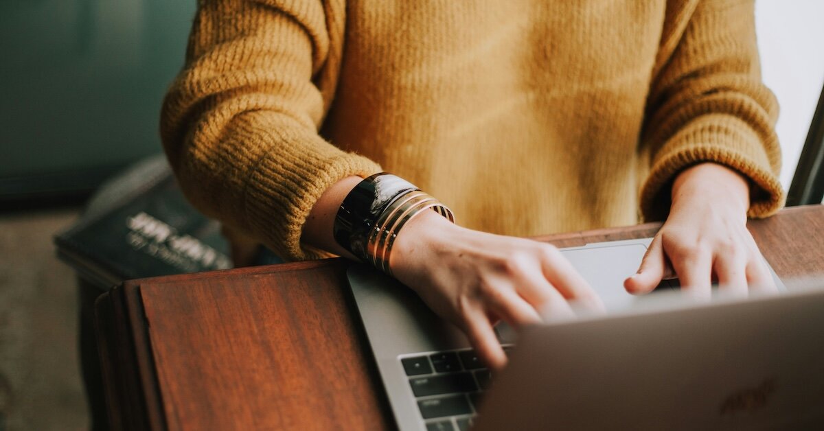 A woman sits at a laptop at a wooden desk