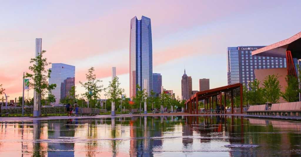 Sunset light frames tall buildings in Oklahoma City with their reflection in a water feature in the foreground