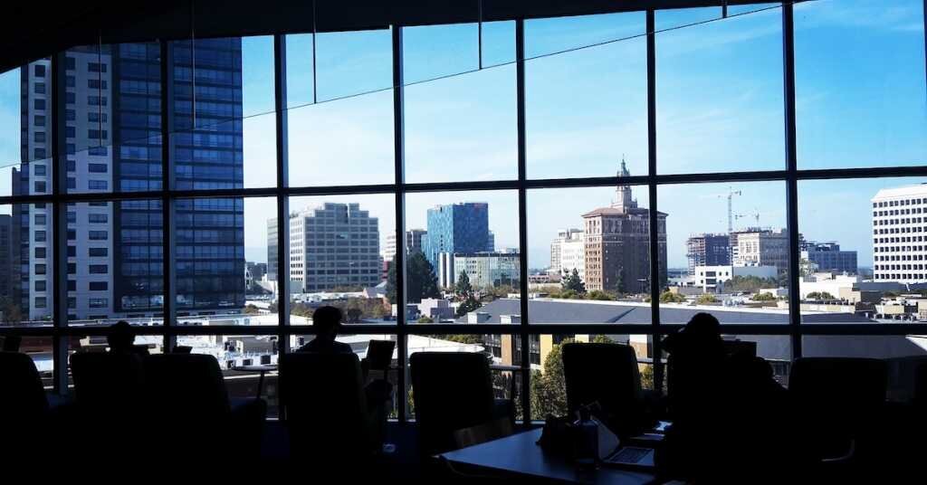 The interior of an office building bullpen in San Jose, looking out on to the city through its windows