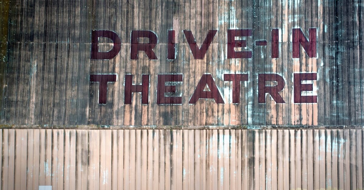 The words "Drive-In Theatre" are painted on an old wooden wall of a building.