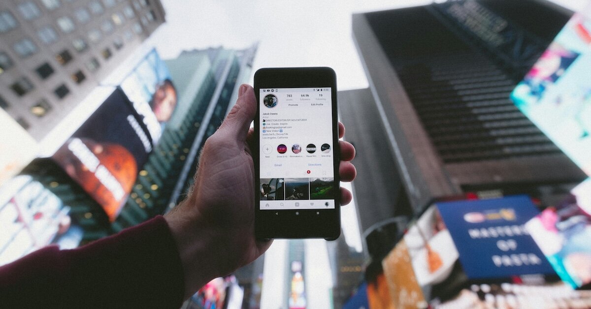 A person holds up a smartphone with Instagram open looking up at the billboards in New York City's Times Square