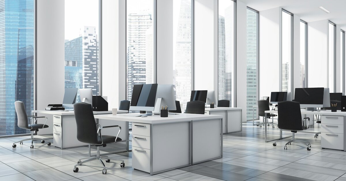 Interior of a brightly lit office building with white desks and computer screens