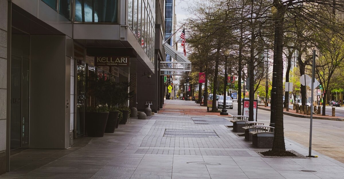 An empty city sidewalk as commercial buildings loom overhead