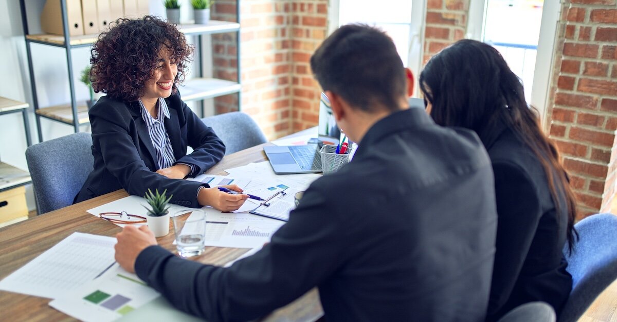 A businesswoman reviews documents with two people sitting across the table