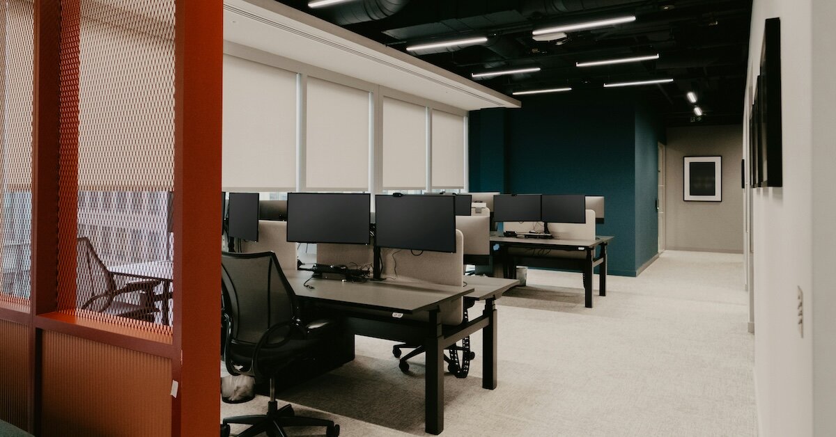 An office bullpen with blue, orange and white walls and floors with computer-laden desks in the center