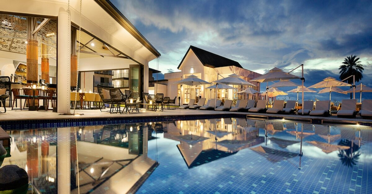 A hotel restaurant with lights and buildings reflecting in the pool in the foreground