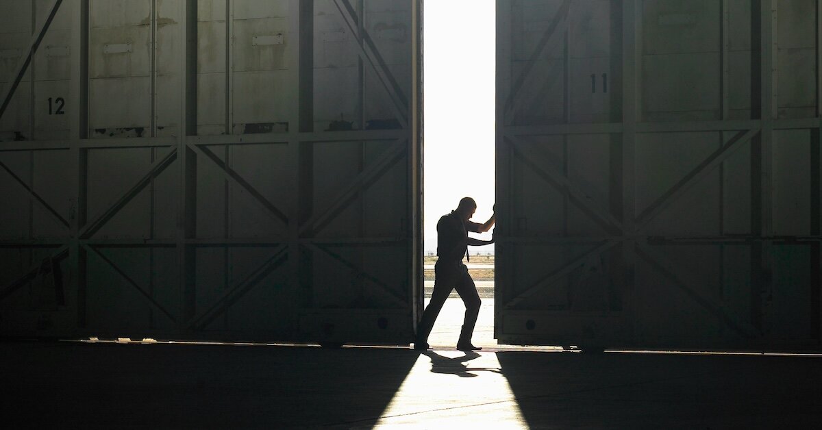 A person opens a dark warehouse to let the sunlight in