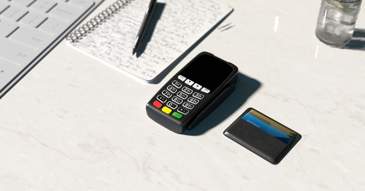 A credit card reader sits next to an open notebook and cardholder wallet on a marble table