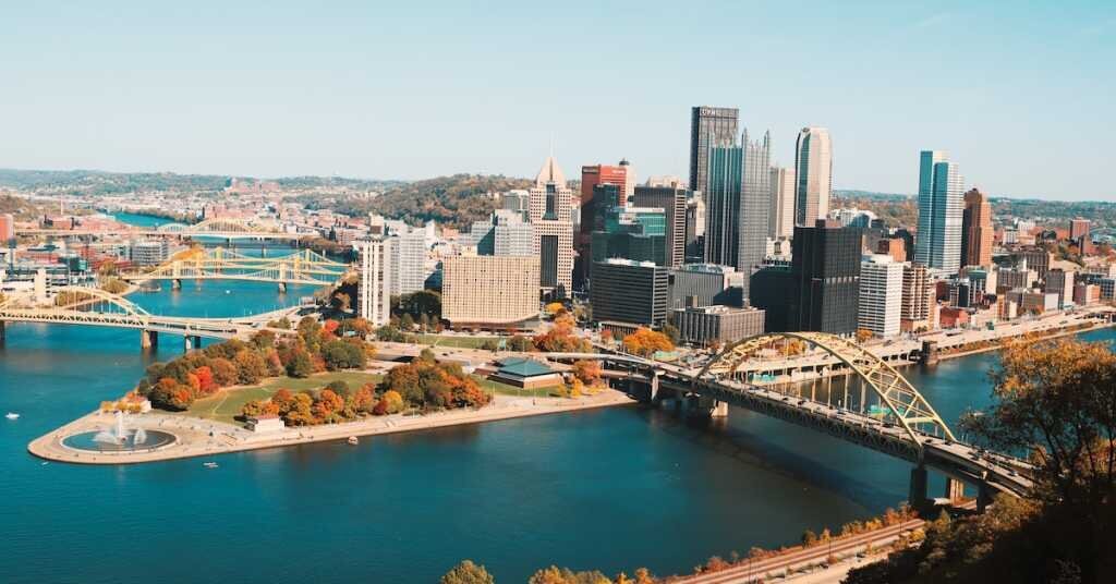 Downtown Pittburgh with a park on the side of the river featuring fall foliage