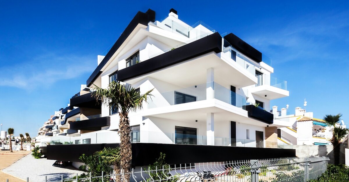 A white and black apartment building stands against the stark blue of the sky