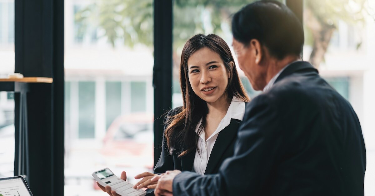 A business professional woman shows a male colleague a figure on a calculator