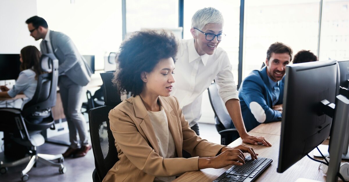 Coworkers look at something at a computer screen in an office setting 