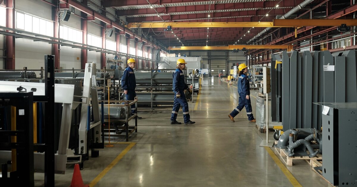 Workers walking around the inside of a factory with hardhats on