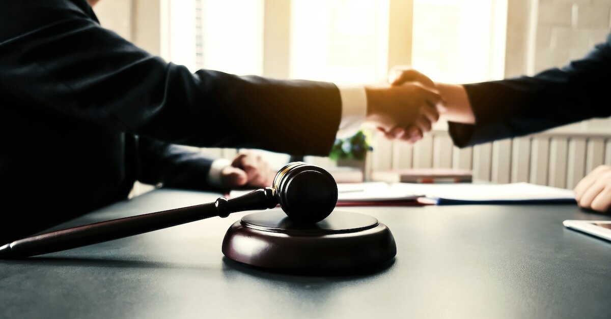 Two people shake hands over a desk with an auction gavel in the foreground