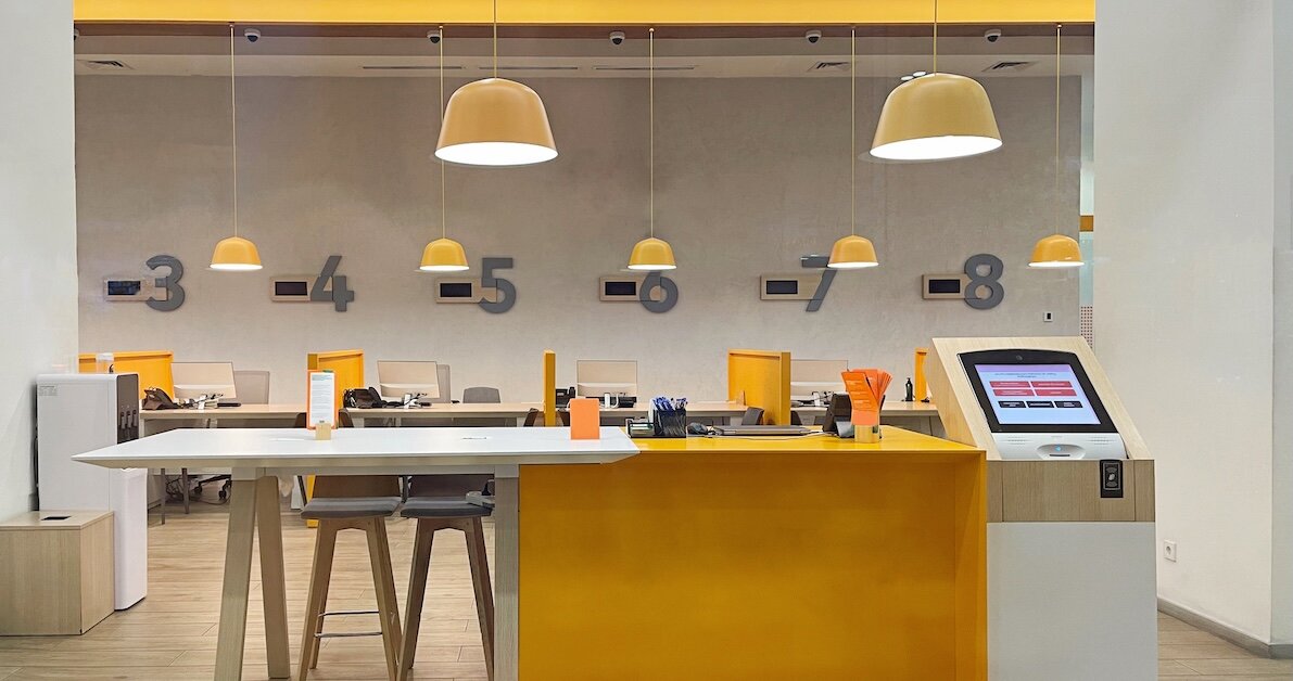 An ATM kiosk with banking stations in a brightly lit, yellow-painted bank