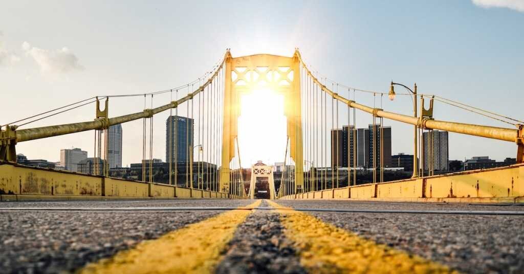 The street of Pittsburgh's bridge with the sun in the background with commercial buildings in the background