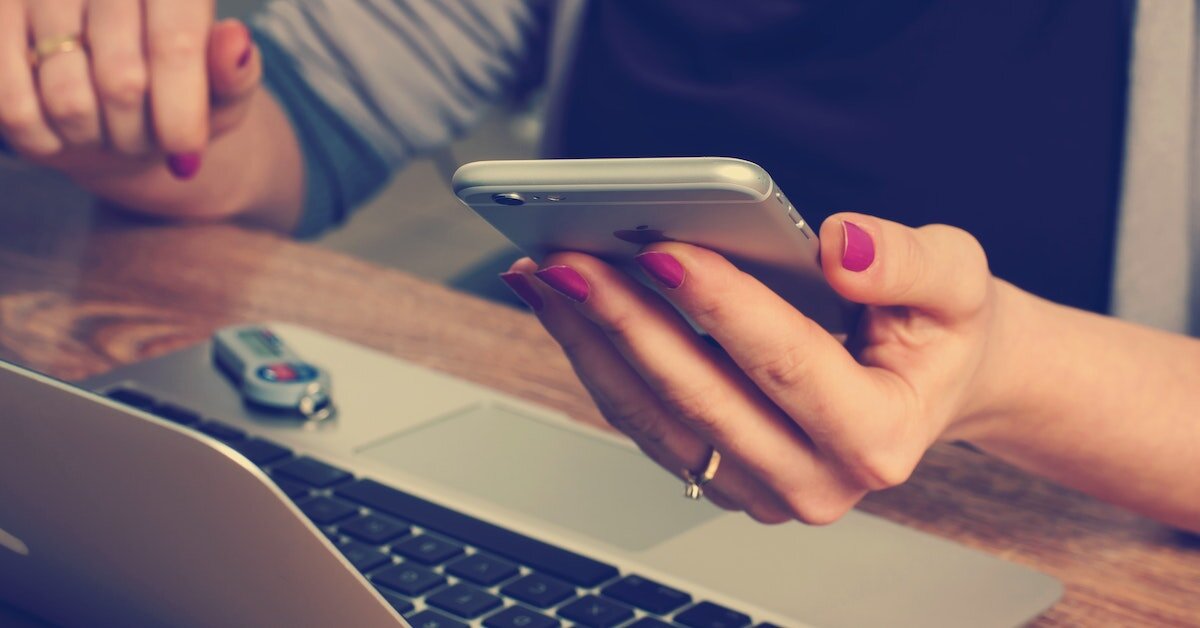 A professional woman checks her phone while working on her laptop