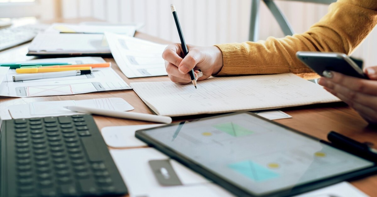 person writing in their notebook next to an ipad with charts