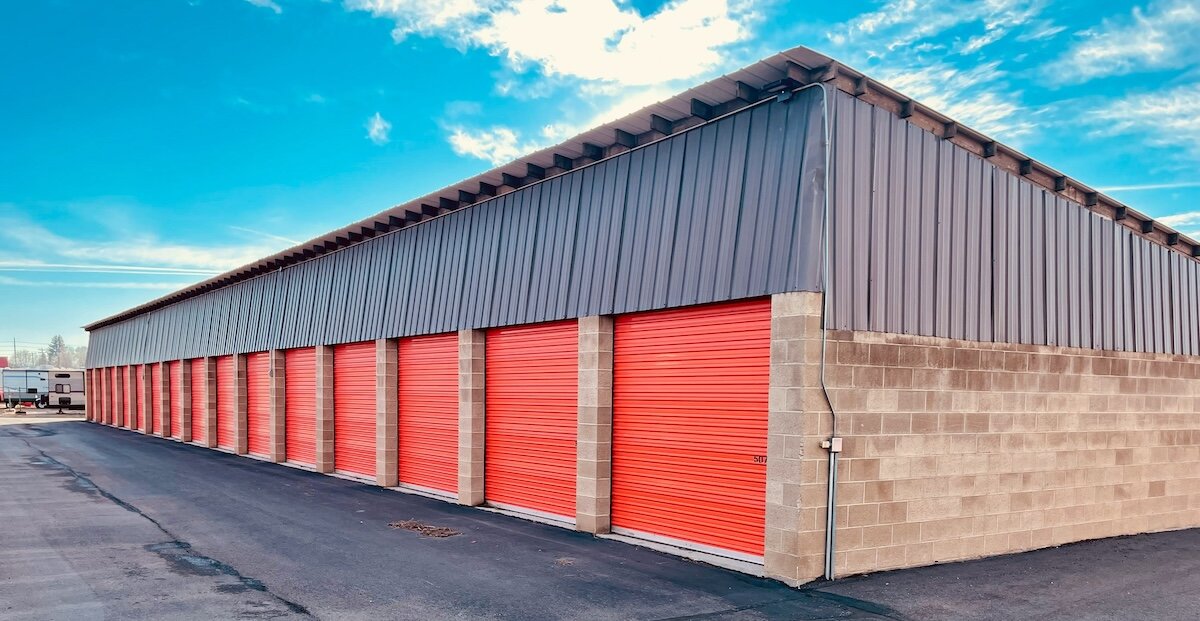 A row of self storage units with red garage doors stands neatly against a blue sky