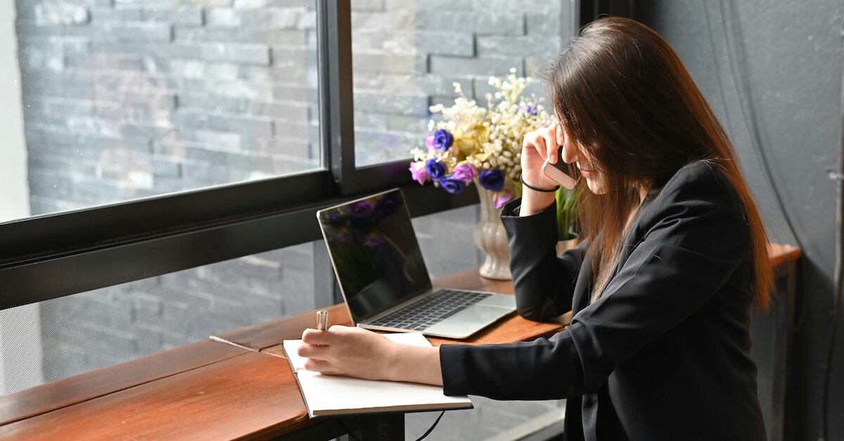 A woman sits at a laptop at a wooden desk