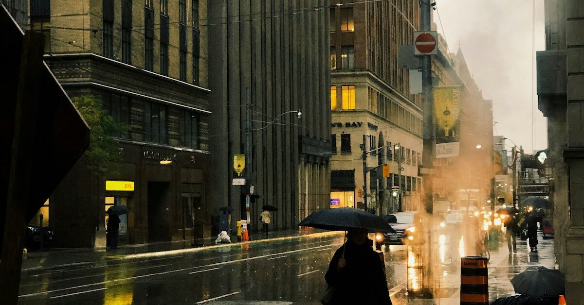 A woman walking down a city street in the rain in October