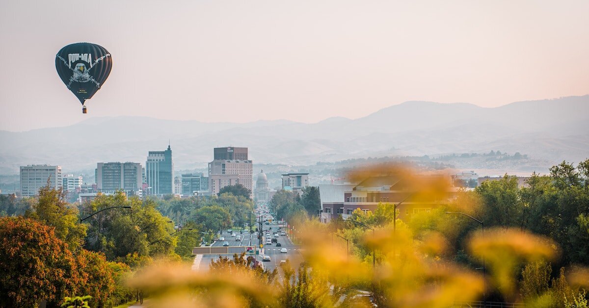 Downtown Boise with fall leaves in the foreground and a hot air balloon floating above the city.
