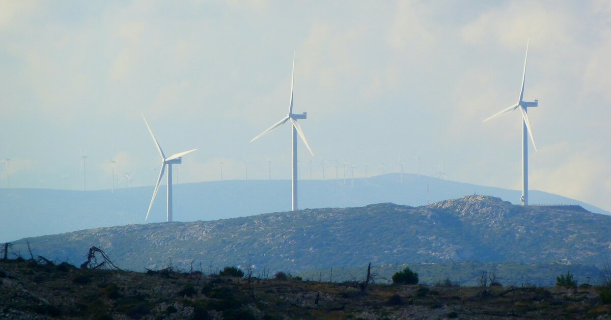 Large wind turbines atop a hill overlooking development sites