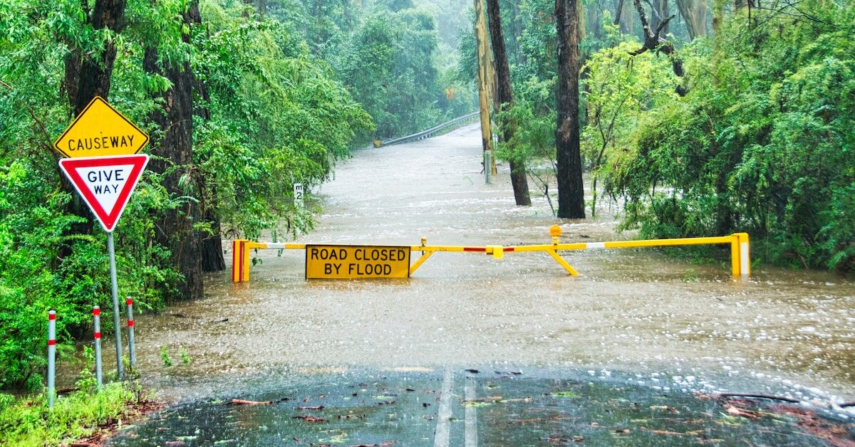 A road is blocked with a gate and sign saying "Road Closed By Flood"