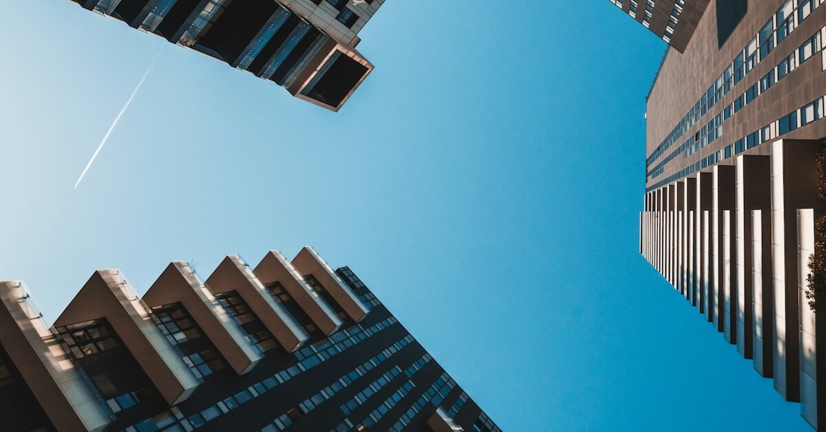 A view of three commercial buildings with an airplane leaving a trail in a blue sky