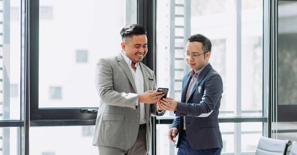 Two men in business attire look at a cell phone's contents together.