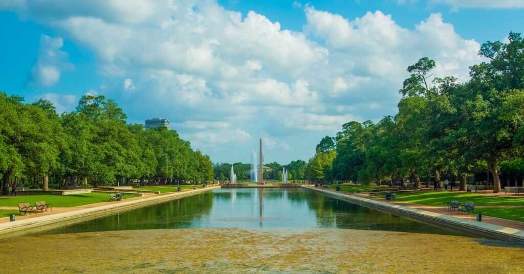 A monument in Houston sits at the far end of a pond in a park