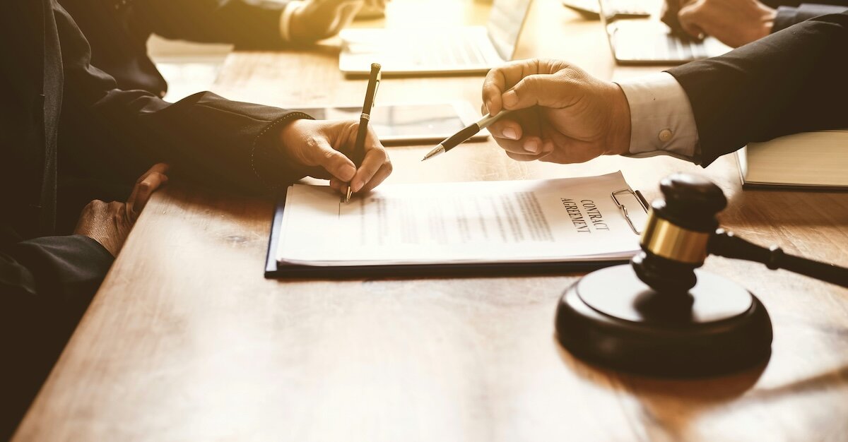 Two people are signing a contract at a desk with an auctioneer's gavel in the foreground