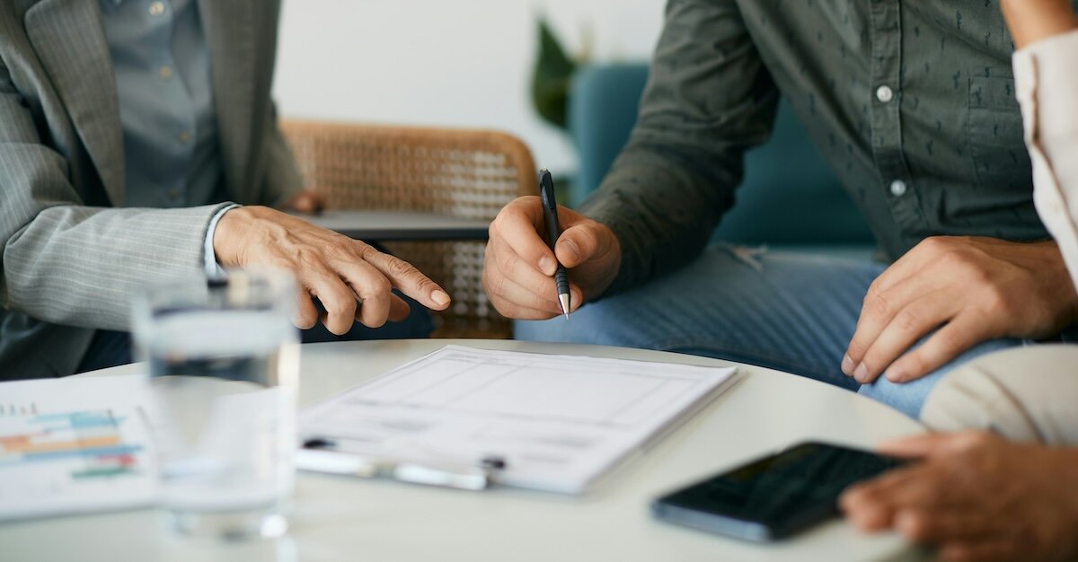 Several people sit around a table reviewing a lease agreement with water, paper, and a phone lying beside them