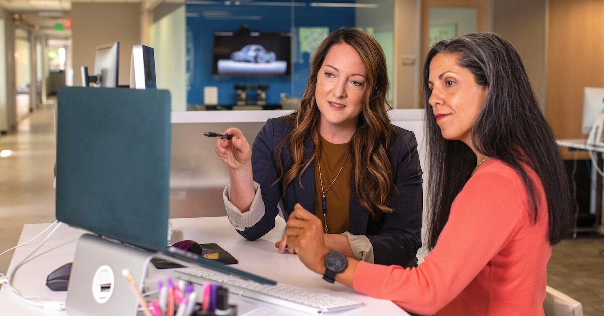 Two women looking at a laptop screen dressed in business casual attire