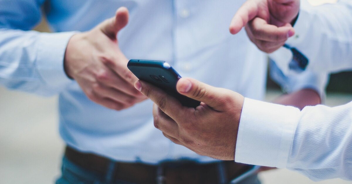 two businessmen gesture to something on the cell phone of one person