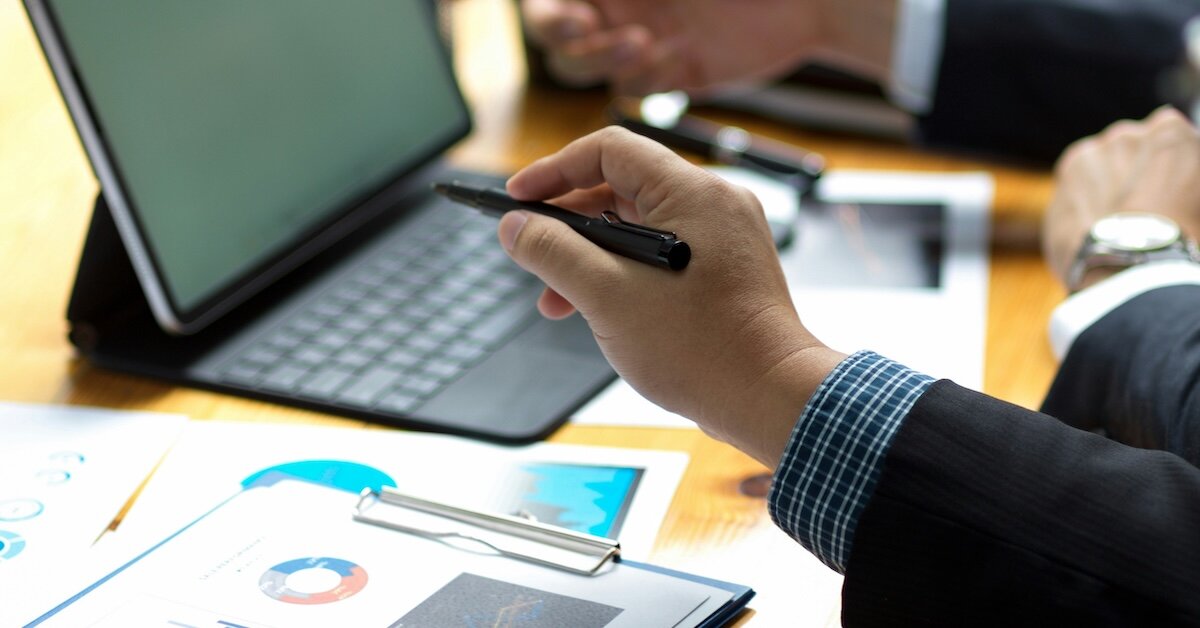 brokers pointing at an ipad next to clipboards of charts and data