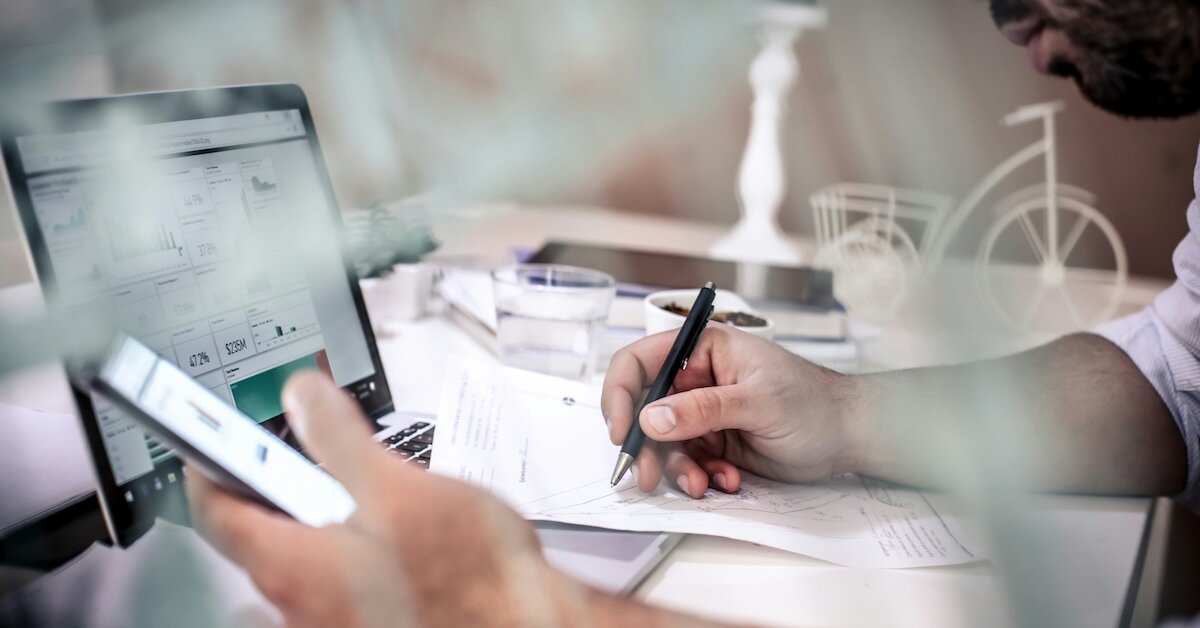 A person bidding at auction online while writing down notes based on something on their phone