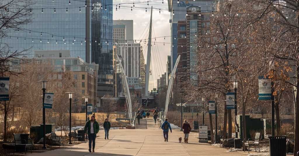 People walking downtown in a park in Denver with a bridge in the background