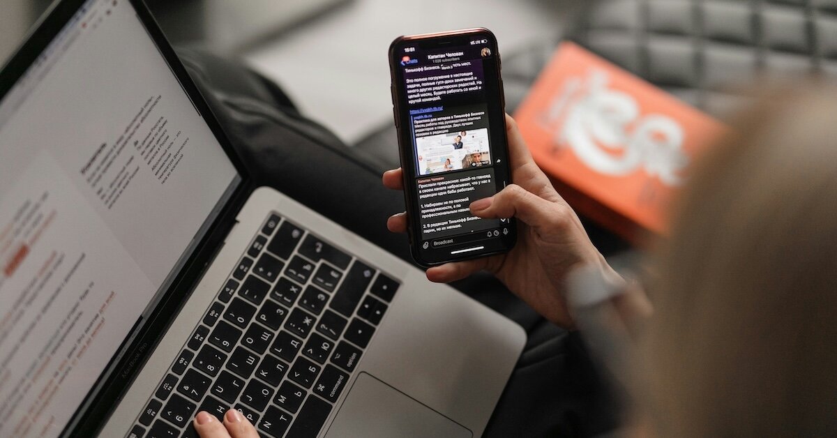 a woman reviewing listing page information on her phone while working on a laptop
