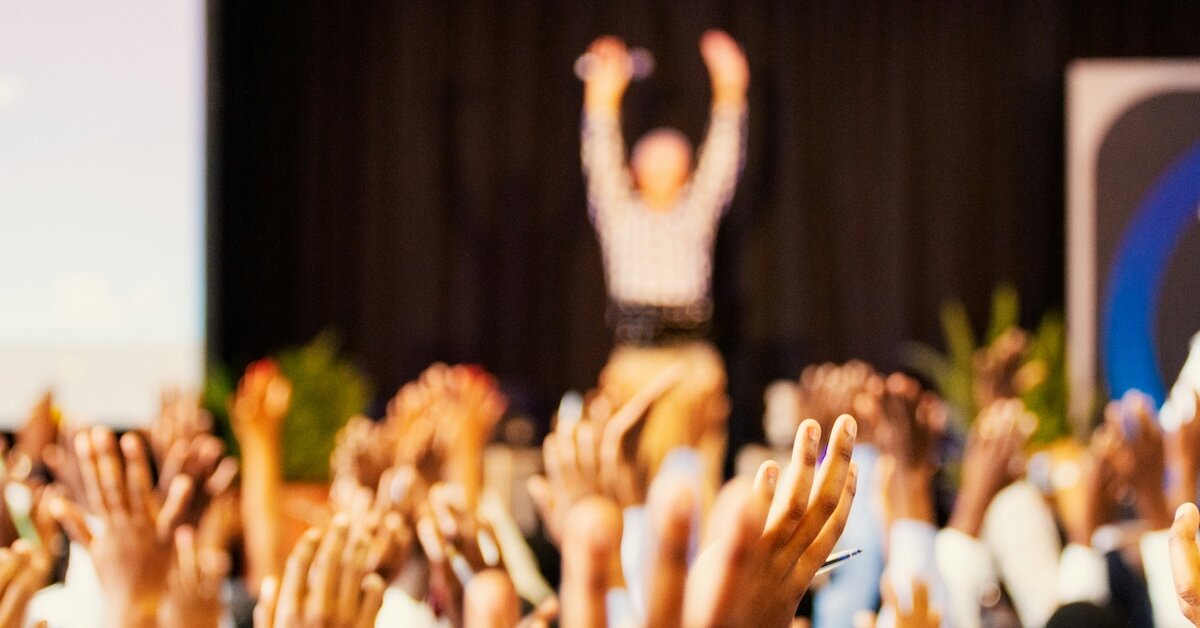 A woman on stage leads a group of women professionals in a conference